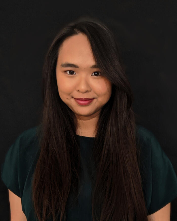 A portrait of Sandy Lam. An Asian American Woman with long, black, straight hair. She has a dark green shirt on and has a black background behind her.