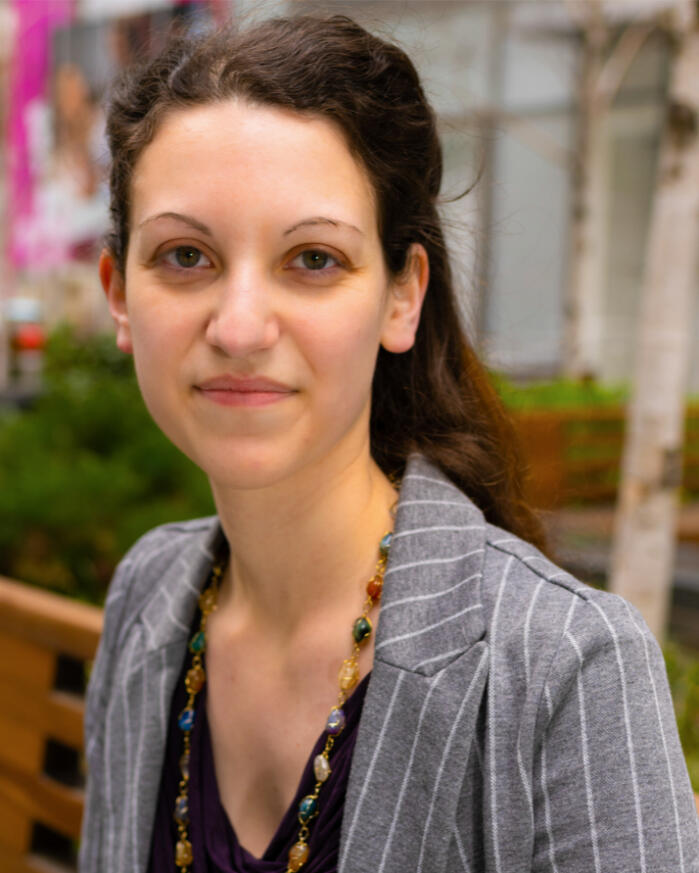 A portrait of Natalie Kane. White woman with brown hair and green eyes, photographed outdoors wearing a blazer.